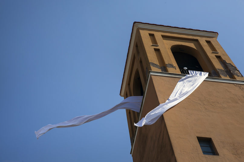White drapes hanging from the church of San Raffaele are moved by the wind on March 19, 2020, in Rome's Trullo neighborhood. The Episcopal Conference invited faithful and religious community to recite the rosary, to display a lighted candle and a white cloth outside the window on the occasion of St. Joseph's feast day. (AP Photo/Alessandra Tarantino)