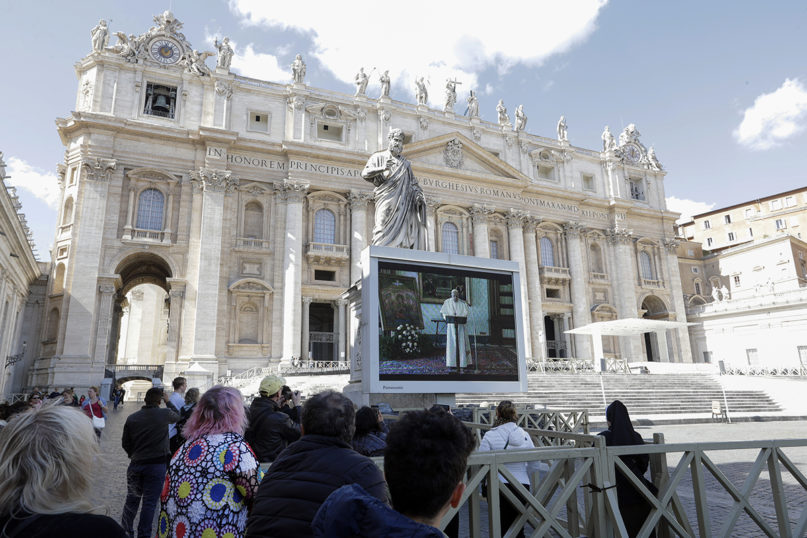 Faithful watch Pope Francis deliver the Angelus prayer on a giant screen to avoid crowds gathering, in St. Peter's Square, at the Vatican, Sunday, March 8, 2020. The pope in his streamed remarks said he was close in prayers to those suffering from the coronavirus and to those caring for them. (AP Photo/Andrew Medichini)