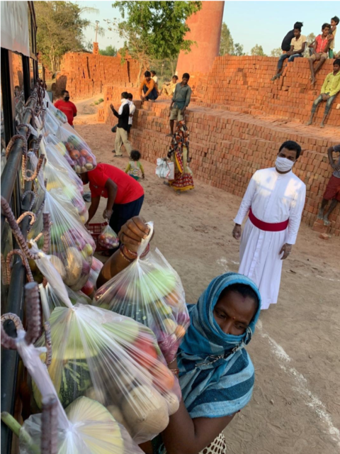 SCHOOL BUS SUSTENANCE: A masked Believers Eastern Church pastor oversees food distribution as hard-hit day laborers in a brick factory community take bags of free food hung on the side of a church school bus.
