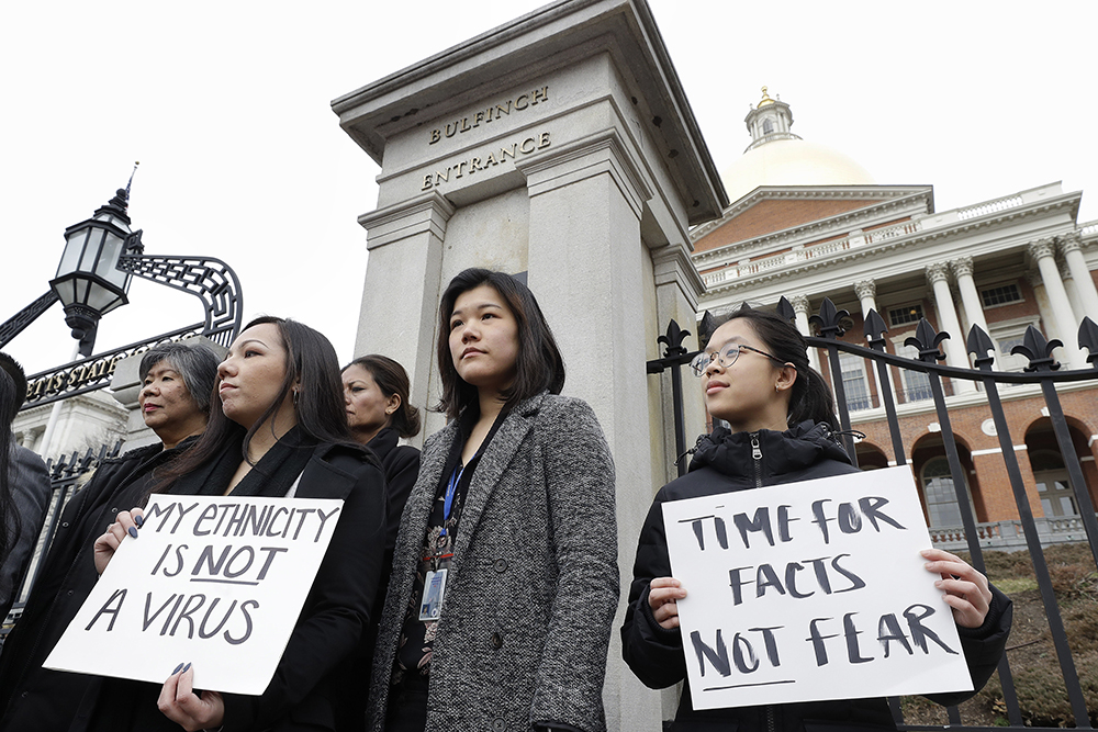 Jessica Wong, of Fall River, Mass., front left, Jenny Chiang, of Medford, Mass., center, and Sheila Vo, of Boston, from the state's Asian American Commission, stand together during a protest, Thursday, March 12, 2020, on the steps of the Statehouse in Boston. Asian American leaders in Massachusetts condemned what they say is racism, fear-mongering and misinformation aimed at Asian American communities amid the widening coronavirus pandemic that originated in China. (AP Photo/Steven Senne)