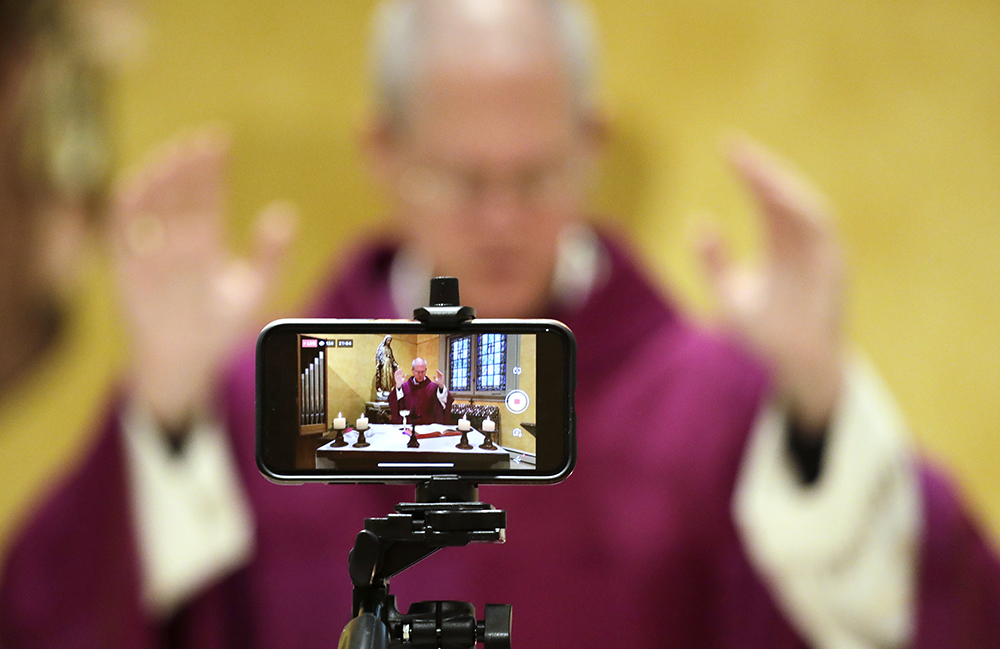A cellphone is used to livestream Mass by Archbishop Paul D. Etienne at St. James Cathedral, the Cathedral for the Catholic Archdiocese of Seattle, where open Masses have been suspended because of the coronavirus outbreak, March 28, 2020, in Seattle. (AP Photo/Elaine Thompson)