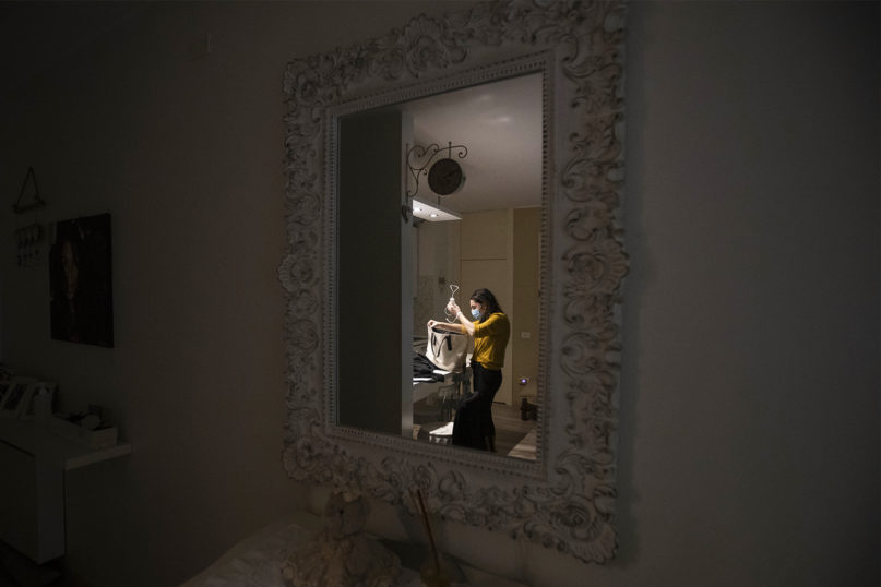 Nurse Cristina Settembrese is reflected in a mirror in her apartment in Basiglio, Italy, as she prepares for her work shift in Milan's San Paolo Hospital, Friday, April 10, 2020. Settembrese spends her days caring for COVID-19 patients in a hospital ward, and when she goes home, her personal isolation begins by her own choice. (AP Photo/Luca Bruno)