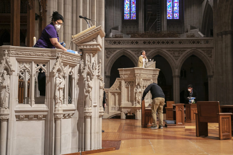 Wearing a face mask, Erlinda Ortega, top left, cleans a pulpit, while Bishop Mariann Edgar Budde, at center, with the Episcopal Diocese of Washington, prepares to record a homily, after Budde led Easter Sunday services via livestream to an empty Washington National Cathedral, April 12, 2020. The large cathedral is normally full on Easter Sunday. (AP Photo/Jacquelyn Martin)