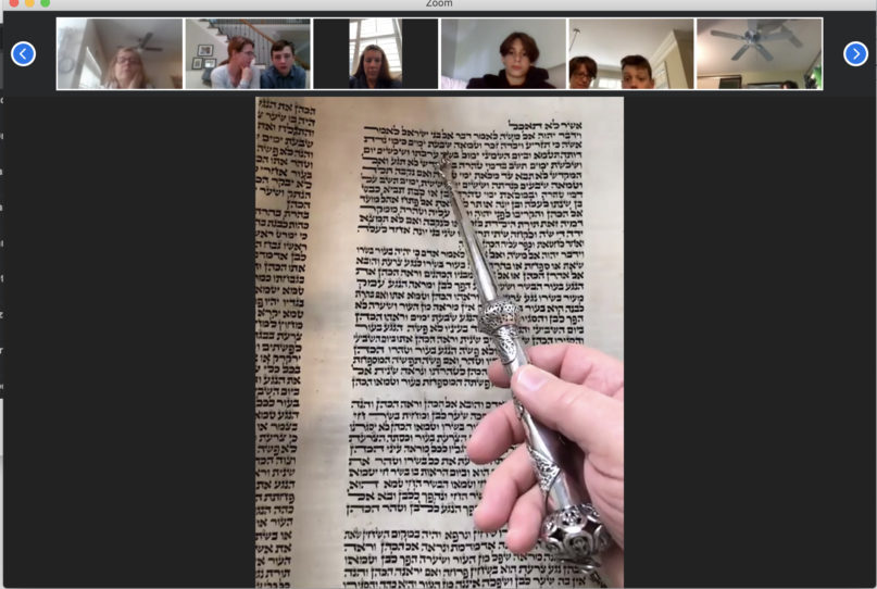 Henry Fuchs holds a “yad,” or silver Torah pointer, to the Tokaj Torah as synagogue members follow along on Zoom, April 25, 2020. Video screenshot by Yonat Shimron