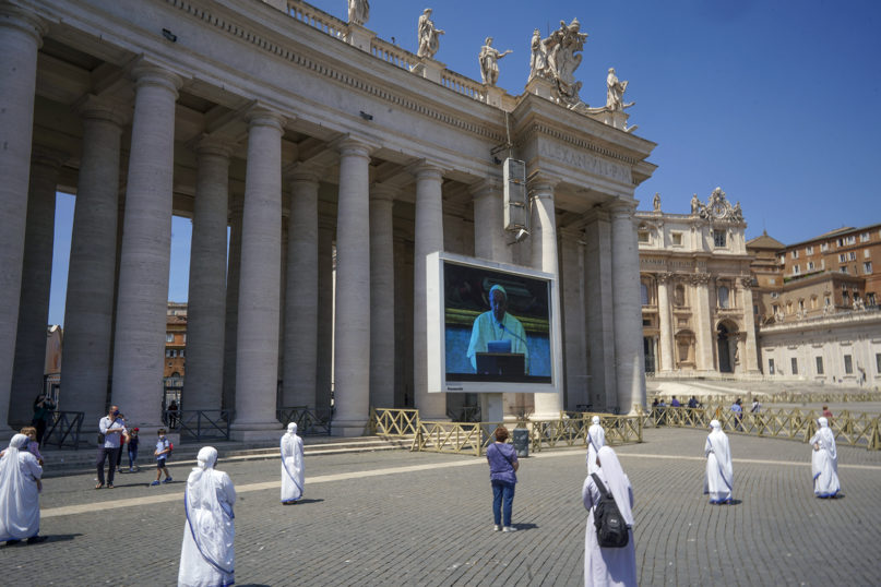 Nuns and faithful respecting social distancing look at Pope Francis reciting the Regina Coeli noon prayer on a giant screen in St. Peter's Square, at the Vatican, Sunday, May 24, 2020. For the first time in months, well-spaced faithful gathered in St. Peter’s Square for the traditional Sunday papal blessing, casting their gaze at the window where the pope normally addresses the faithful, since the square had been closed due to anti-coronavirus lockdown measures.  (AP Photo/Andrew Medichini)