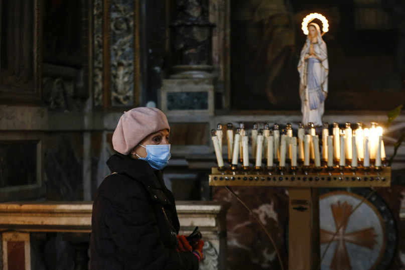 A woman passes candles at the Santa Maria ai Monti church in Rome on March 29, 2020. Priests will have to wear protective masks and gloves while giving Catholics Communion and be careful not to touch the hands of the faithful when public Masses resume in Italy on May 18, as the country slowly eases some lockdown measures. Avvenire, the daily newspaper of the Italian Catholic Bishops Conference, provided details of an accord that Premier Giuseppe Conte reached with church officials to allow the faithful to return to Mass during the COVID-19 pandemic. (Cecilia Fabiano/LaPresse via AP, File)