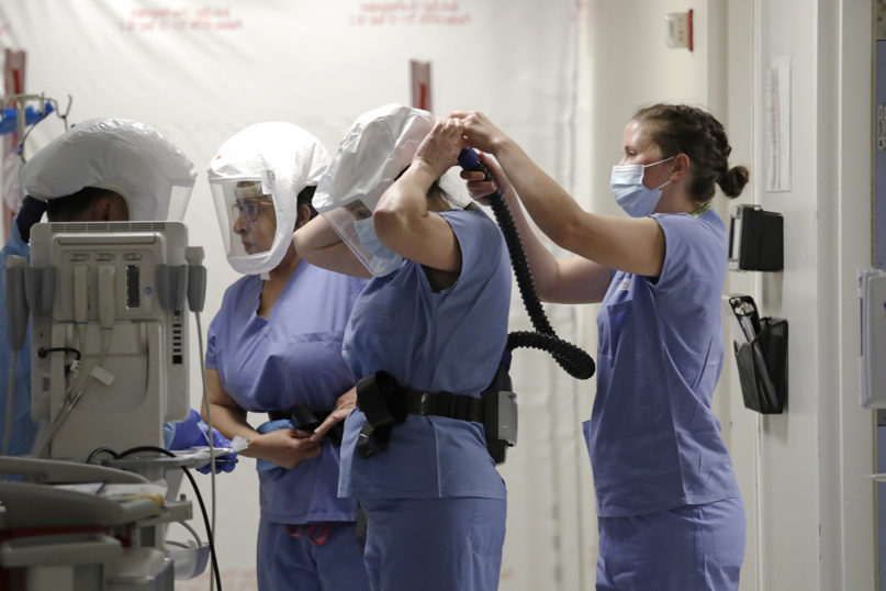 Medical staff workers put on protective equipment, including powered air purifying respirators with air tubes connected between a pack worn on their waist and a hood, before heading into a patient room in the COVID-19 intensive care unit at Harborview Medical Center on May 8, 2020, in Seattle. (AP Photo/Elaine Thompson)