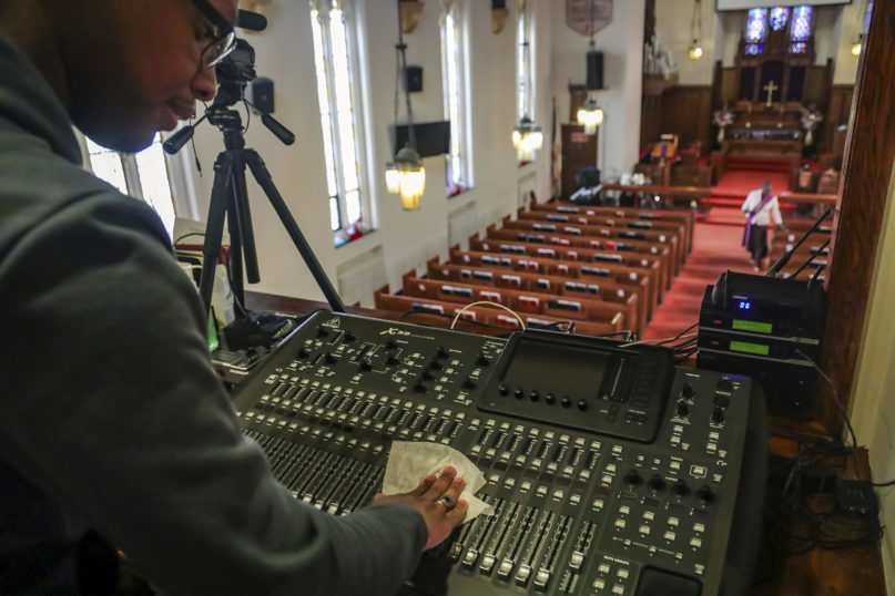Multimedia technician Joseph Stoute, 21, uses a disinfectant wipe to clean the audio equipment at St. Paul’s Methodist Church in Brooklyn, N.Y., where he directed a livestream online broadcast for home-bound congregants due to citywide restrictions aimed at controlling the COVID-19 outbreak, March 22, 2020, in New York. (AP Photo/Bebeto Matthews)