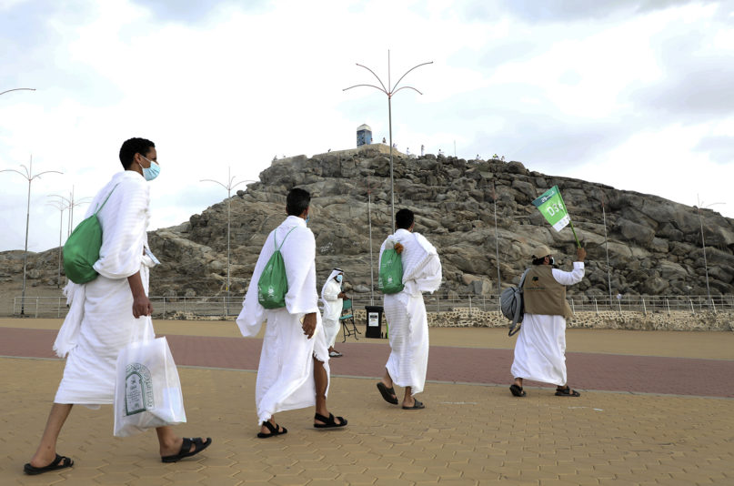 Muslim pilgrims walk towards the rocky hill known as Mount Arafat, background, as they practice social distancing to protect against coronavirus during the annual hajj pilgrimage near the holy city of Mecca, Saudi Arabia, Thursday, July 30, 2020. This year's hajj was dramatically scaled down from 2.5 million pilgrims to as few as 1,000 due to the coronavirus pandemic. (AP Photo)