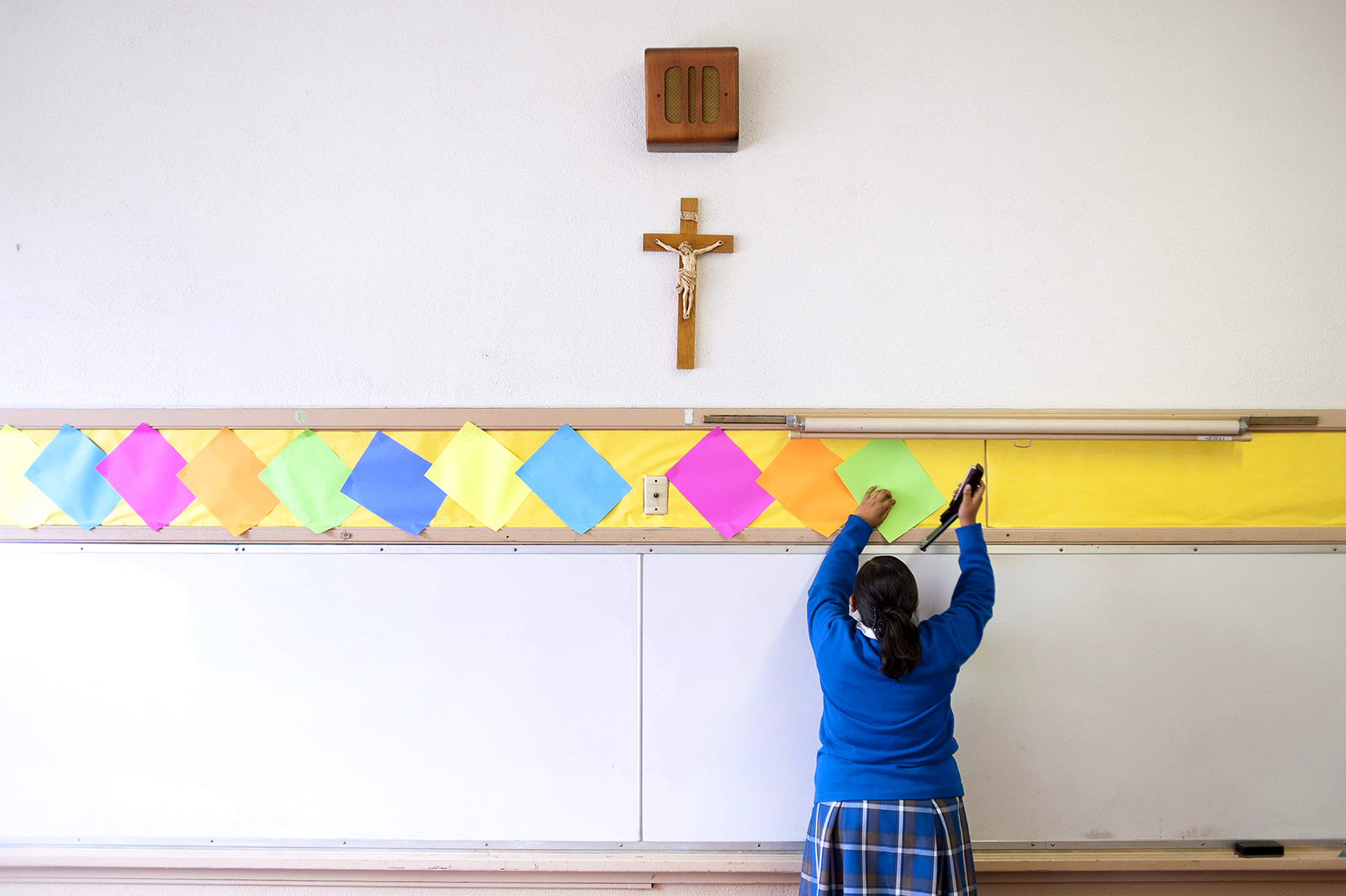 This July 18, 2012, file photo shows a student stapling colored paper to the wall of a classroom after summer school at Our Lady of Lourdes in Los Angeles. (AP Photo/Grant Hindsley)