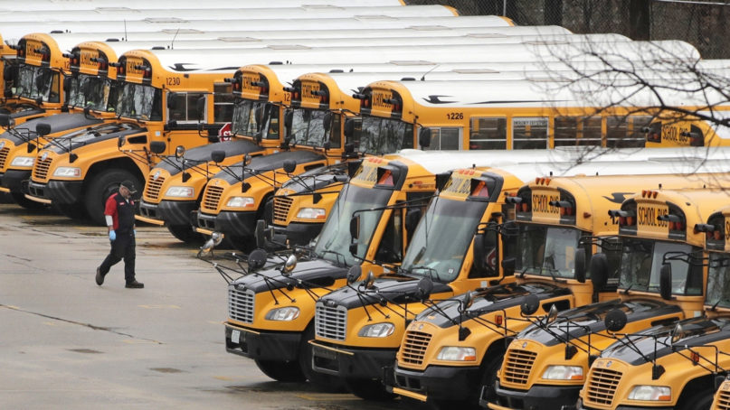 In this April 27, 2020, file photo, a worker passes public school buses parked at a depot in Manchester, New Hampshire. As the Trump administration pushes full steam ahead to force schools to resume in-person education, public health experts warn that a one-size-fits-all reopening could drive infection and death rates even higher. (AP Photo/Charles Krupa, File)