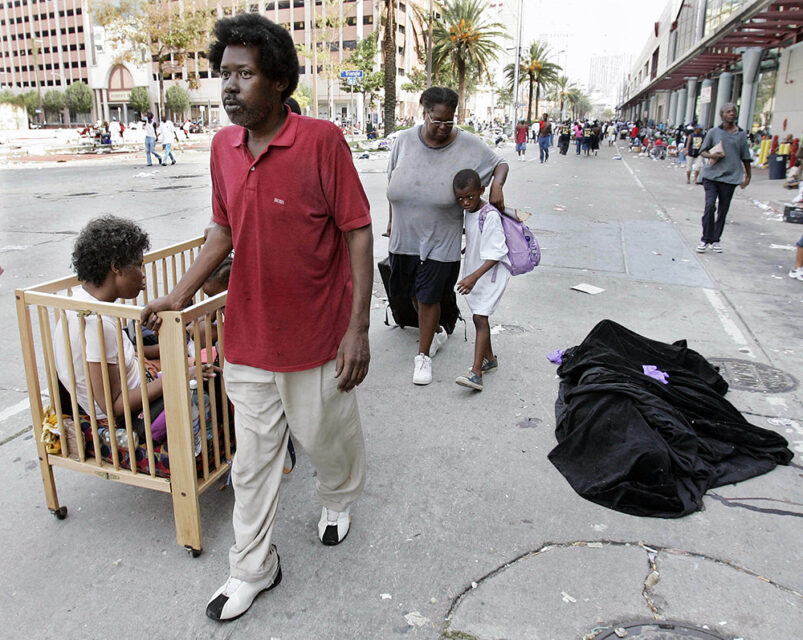 FILE - In this Sept. 3, 2005 file photo, a family of Hurricane Katrina victims walks past the covered body of 45-year-old Danny Brumfield in front of the convention center in New Orleans. (AP Photo/Eric Gay, File)