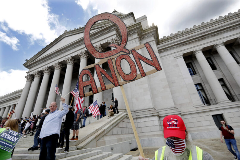 A demonstrator holds a QAnon sign as he walks at a protest opposing Washington state’s stay-at-home order to slow the coronavirus outbreak April 19, 2020, in Olympia, Washington. Washington Gov. Jay Inslee had blasted then-President Donald Trump’s calls to “liberate” parts of the country from stay-at-home and other orders designed to combat the spread of the coronavirus. Inslee said Trump was fomenting a potentially deadly “insubordination” among his followers before the pandemic is contained. (AP Photo/Elaine Thompson)