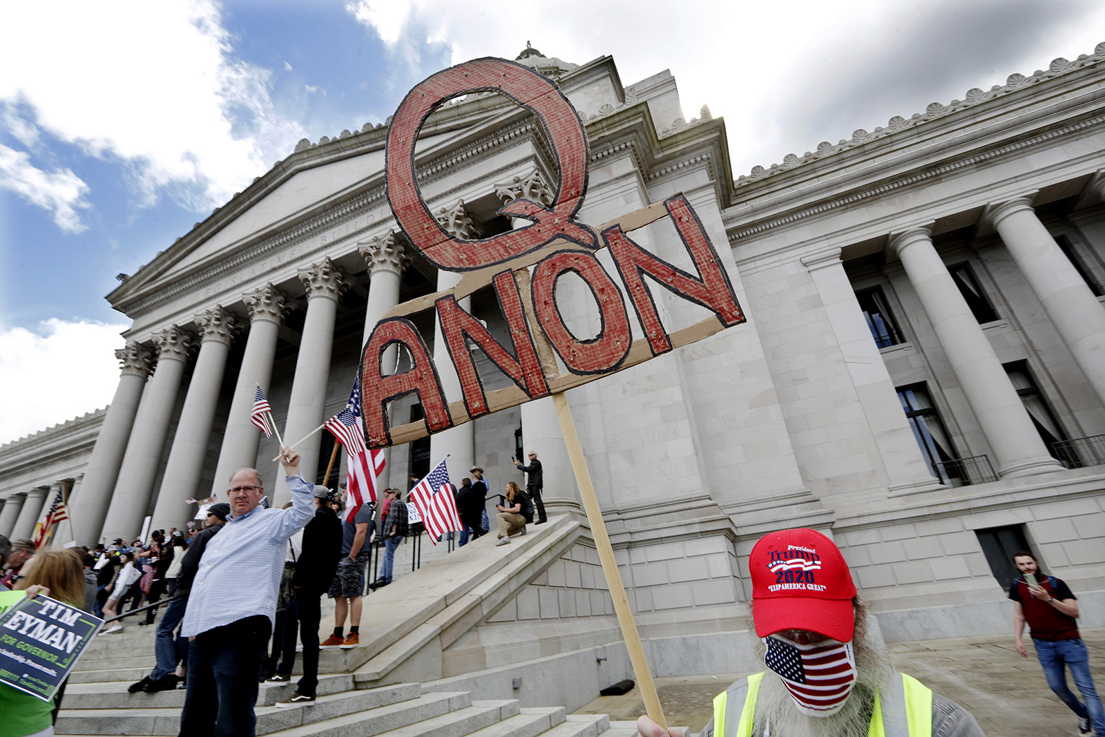 A demonstrator holds a QAnon sign as he walks at a protest opposing Washington state’s stay-at-home order to slow the coronavirus outbreak April 19, 2020, in Olympia, Washington. Washington Gov. Jay Inslee had blasted President Donald Trump’s calls to “liberate” parts of the country from stay-at-home and other orders designed to combat the spread of the coronavirus. Inslee said Trump was fomenting a potentially deadly “insubordination” among his followers before the pandemic is contained. (AP Photo/Elaine Thompson)