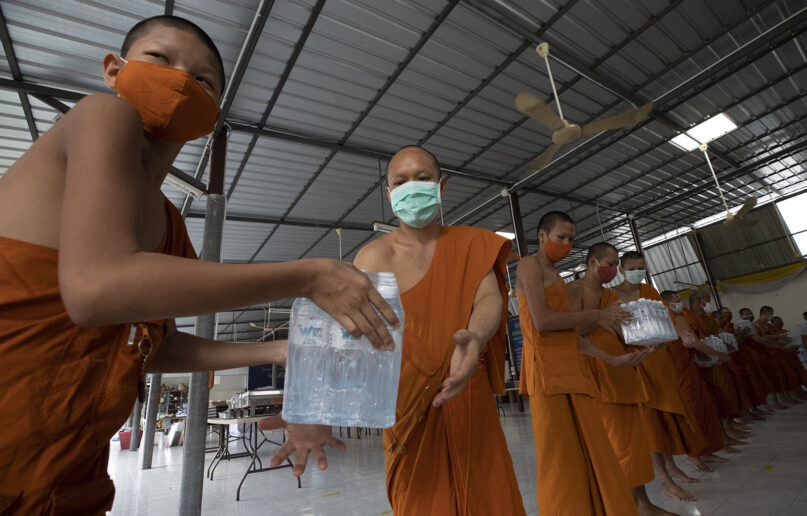 Thai Buddhist monks wearing face masks to protect themselves from the coronavirus pass packs of water after their devotees donated water to Molilokayaram temple in Bangkok, Thailand, Friday, April 17, 2020. (AP Photo/Sakchai Lalit)