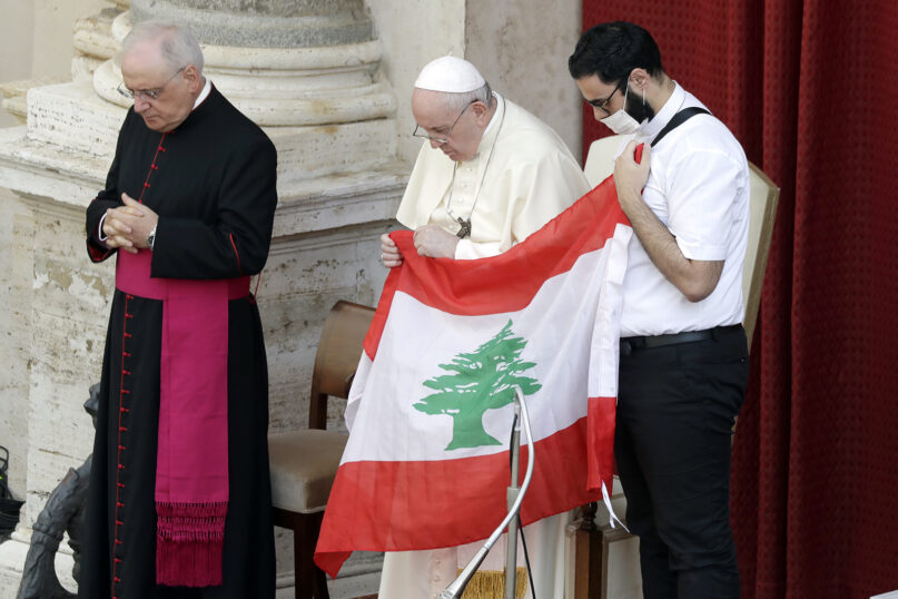 Pope Francis is flanked by Lebanese priest Georges Breidi, right, as they hold a Lebanese flag in remembrance of last month’s explosion in Beirut, during the pontiff’s general audience, the first with faithful since February when the coronavirus outbreak began, at the San Damaso courtyard at the Vatican on Sept. 2, 2020. (AP Photo/Andrew Medichini)
