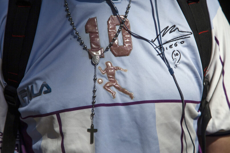 A man, wearing a jersey honoring Diego Maradona and a rosary, waits in a line outside the presidential palace to pay his last respects, in Buenos Aires, Argentina, Thursday, Nov. 26, 2020. The Argentine soccer great, who was among the best players ever and who led his country to the 1986 World Cup title, died from a heart attack at his home Wednesday, at the age of 60. (AP Photo/Maria Paula Avila)