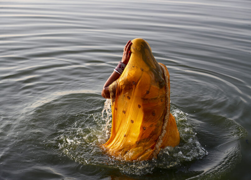 A Hindu devotee takes a dip while praying to the sun god, standing in knee-deep waters, in Hussain Sagar Lake during the Chhath Puja festival in Hyderabad, India, Nov. 20, 2020. (AP Photo/Mahesh Kumar A.)