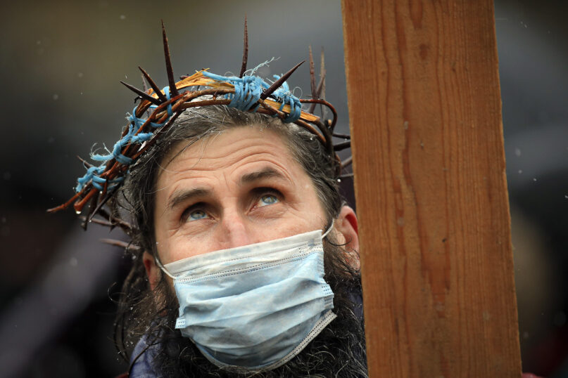 A man wearing a crown of thorns holds a wooden cross while attending a religious service celebrating St. Andrew in the village of Ion Corvin, eastern Romania, Monday, Nov. 30, 2020. Braving wintry weather and the new coronavirus fears, several hundred Orthodox Christian believers gathered outside a cave in eastern Romania where St. Andrew is said to have lived and preached in the 1st century. (AP Photo/Vadim Ghirda)