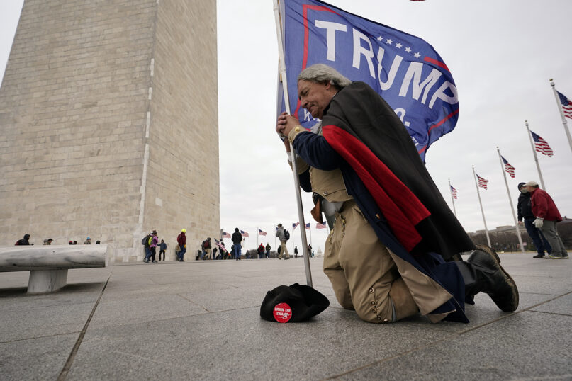 A man dressed in Colonial-era attire kneels and prays near the Washington Monument with a Trump flag on Jan. 6, 2021, in Washington. (AP Photo/Carolyn Kaster)