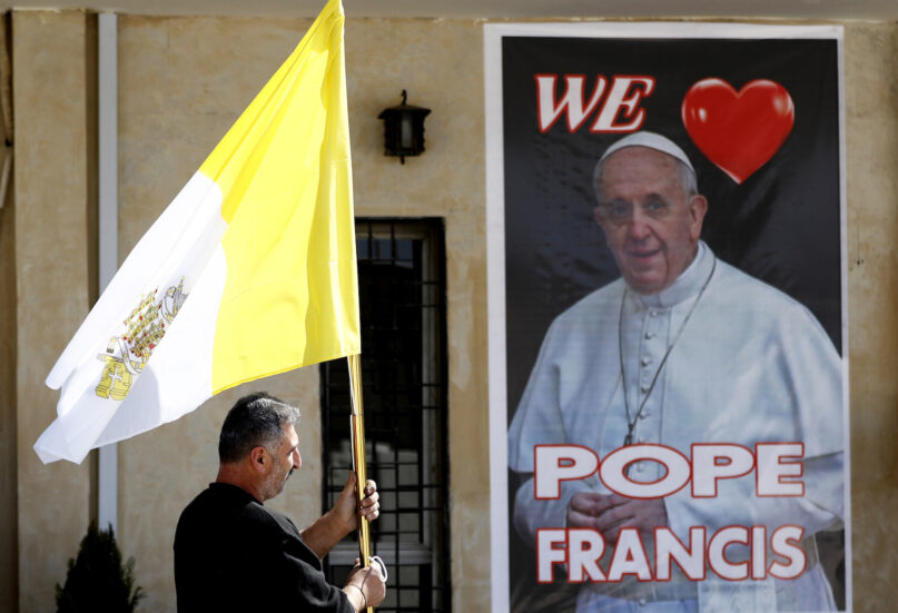A Christian priest Places a poster of the Pope Francis and a Vatican flag during preparations for the Pope's visit in Mar Youssif Church in Baghdad, Iraq, Friday, Feb. 26, 2021. (AP/Photo/Hadi Mizban)