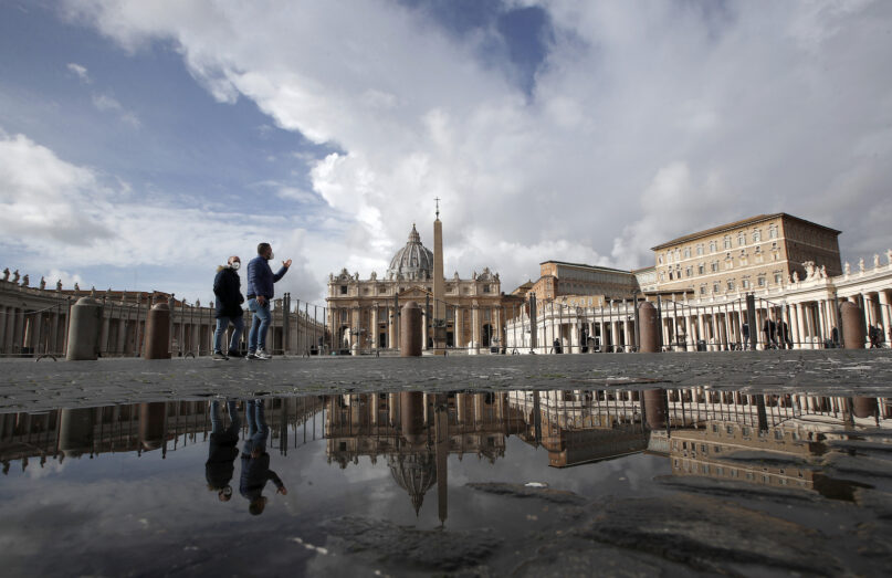 In this Jan. 31, 2021, file photo, people are reflected on a puddle as they walk in St. Peter's Square at the Vatican. The Vatican's trial began July 27, 2021, addressing charges of 10 individuals regarding a real estate deal using Vatican funds. (AP Photo/Alessandra Tarantino, File)