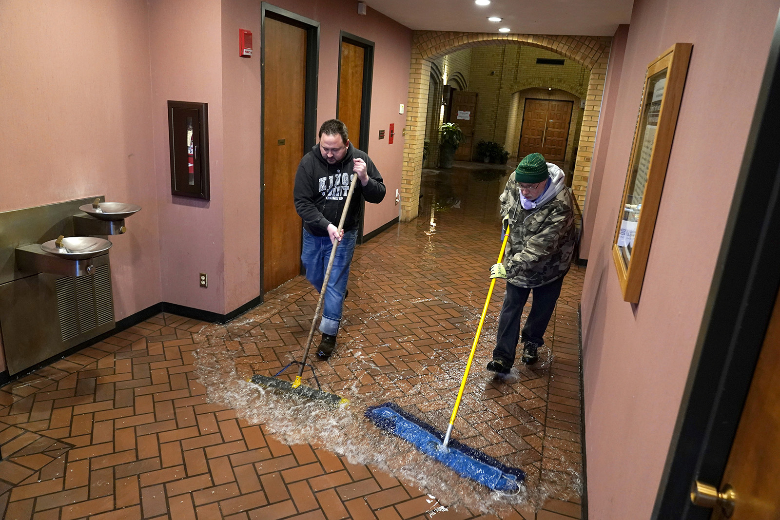 The Rev. John Szatkowski, left, and Deacon Bob Bonomi sweep water out of St. Paul The Apostle Church in Richardson, Texas, Wednesday, Feb. 17, 2021. Father Szatkowski and his staff found the flooding, from a broken water line, as they prepared for Ash Wednesday services. (AP Photo/Tony Gutierrez)