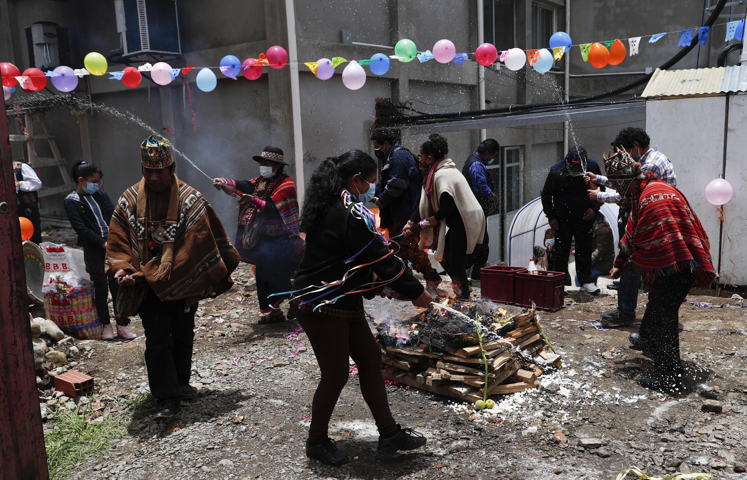 People spray the ground with beer as they celebrate "Martes de Challa,” or Challa Tuesday, in which devotees bury food, throw candies, burn incense, decorate their houses, businesses, cars, all in a show of gratitude to Pachamama or Mother Earth, in La Paz, Bolivia, Tuesday, Feb. 16, 2021. The Andean ritual coincides with the Christian holiday Shrove Tuesday, culminating with Carnival festivities to prepare for the Lenten season which begins Ash Wednesday, the following day. (AP Photo/Juan Karita)