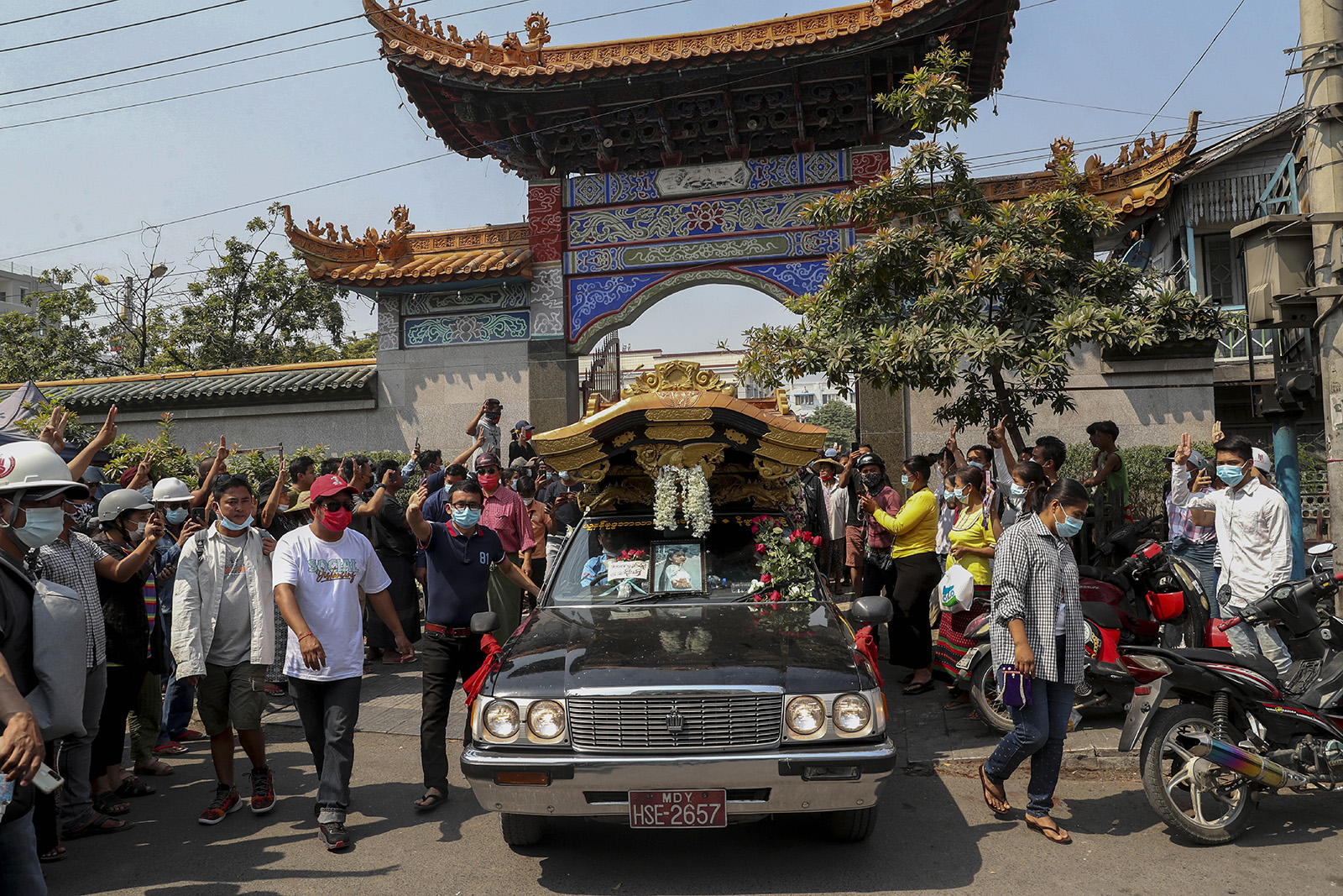 Bystanders flash a three-fingered sign of resistance as the body of Kyal Sin, also known by her Chinese name Deng Jia Xi, is driven out from the Yunnan Chinese temple in Mandalay, Myanmar, Thursday, March 4, 2021. Kyal Sin was shot in the head by Myanmar security forces during an anti-coup protest rally she was attending Wednesday. (AP Photo)