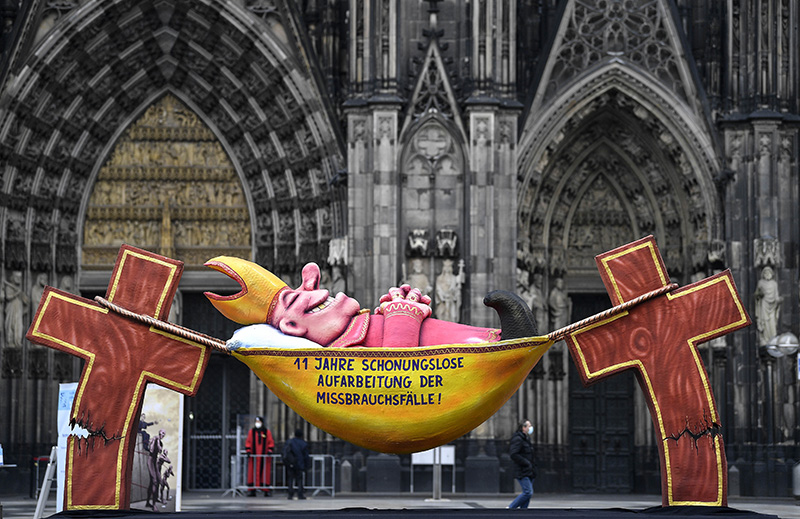 A carnival float depicting a sleeping Cardinal, reading '11 years of relentless processing of cases of abuse' is set in front of the Cologne Cathedral to protest against the Catholic Church in Cologne, Germany, Thursday, March 18, 2021. Faced with accusations of trying to cover up sexual violence in Germany's most powerful Roman Catholic diocese, the archbishop of Cologne Cardinal Rainer Maria Woelki will publish an independent investigation. (AP Photo/Martin Meissner)