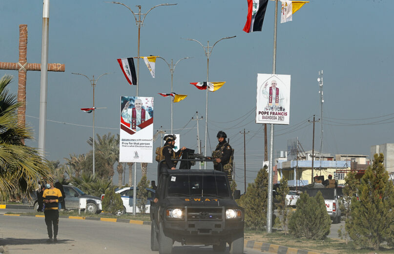 Iraqi security forces pass by Iraqi and the Vatican flags, and posters announcing the upcoming visit of Pope Francis, in a street in Qaraqosh, Iraq, Monday, Feb. 22, 2021. (AP/Photo/Hadi Mizban)