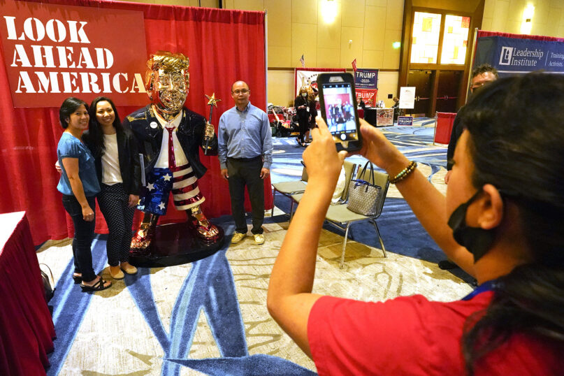 Conference attendees pose for a photo next to a statue of former President Donald Trump at the merchandise show at the Conservative Political Action Conference (CPAC), Saturday, Feb. 27, 2021, in Orlando, Fla. (AP Photo/John Raoux)