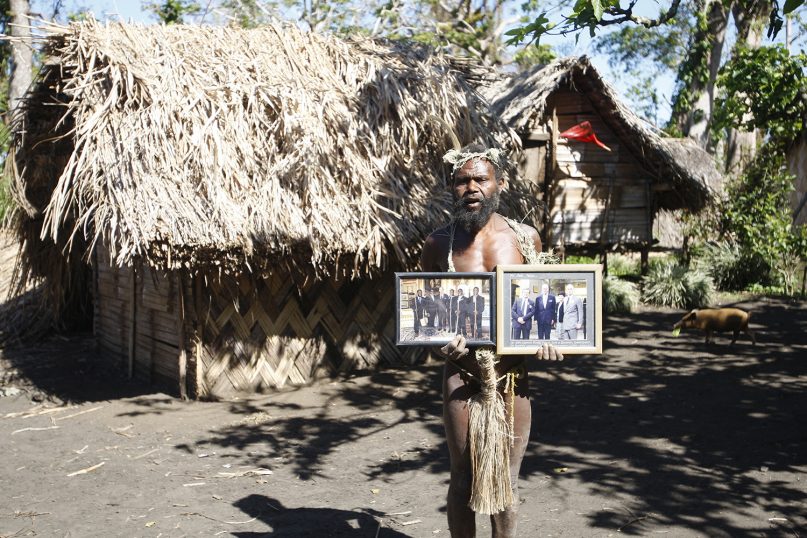 In this Sunday, May 31, 2015 photo, Albi Nagia poses with photographs of Prince Philip in Yakel, Tanna island, Vanuatu. Nagia is part of a movement which worships the prince as the son of their ancestral God. (AP Photo/Nick Perry)