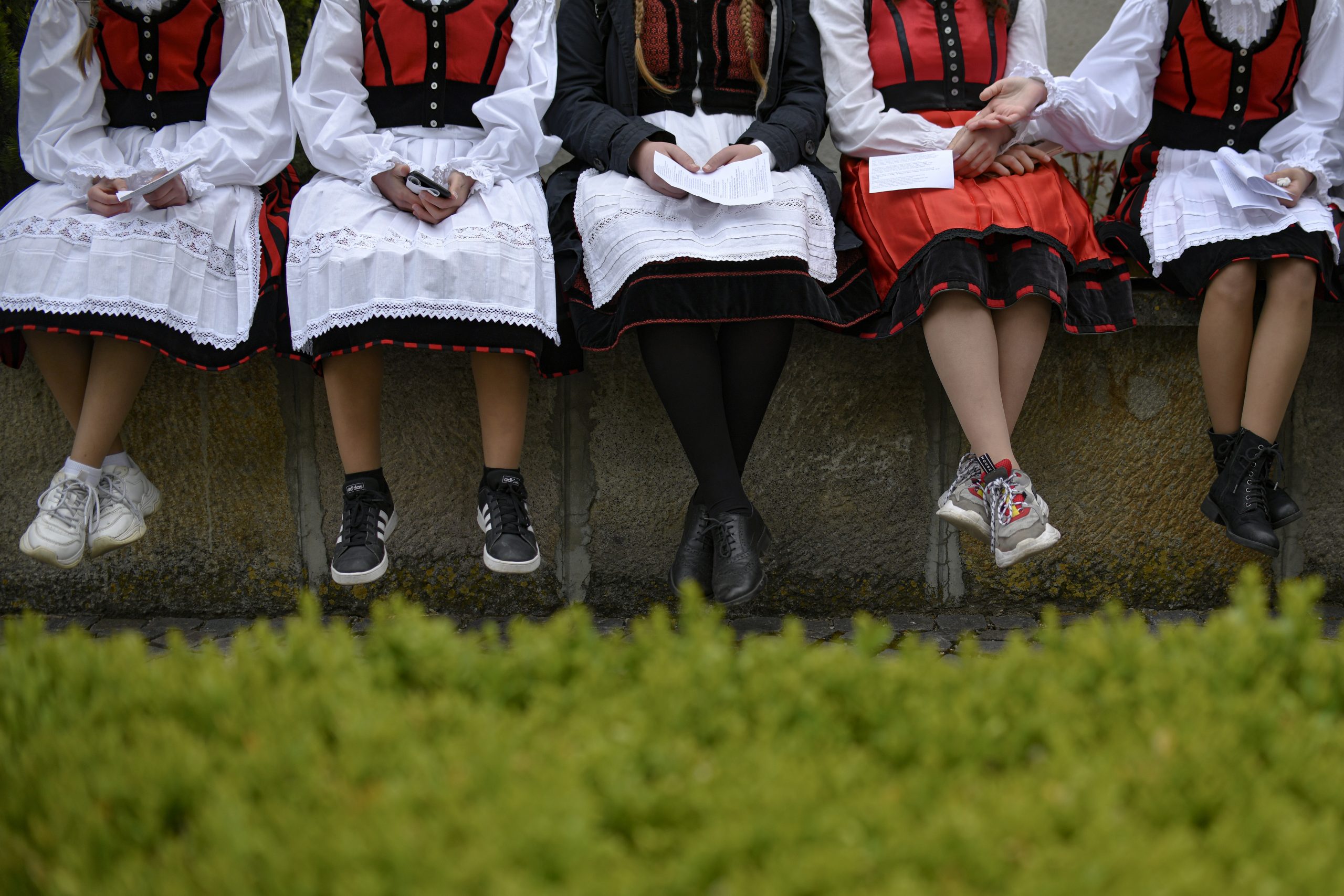 Girls dressed in traditional outfits rest during a Catholic pilgrimage attended by tens of thousands of people who joined the biggest religious event of their faith, in Sumuleu Ciuc, Romania on Saturday, May 22, 2021. Over 35,000 Catholic pilgrims gathered at an open-air shrine in Sumuleu Ciuc in Transylvania on Saturday for a centuries-old procession that was canceled last year due to the coronavirus pandemic.  (AP Photo / Andreea Alexandru)