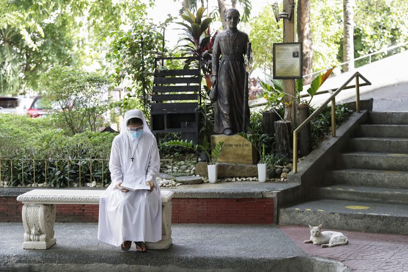 A Catholic nun wearing a protective mask reads outside the Immaculate Heart of Mary Parish Church that turned into a temporary vaccination center in Quezon City, Philippines on Friday, May 21, 2021. Philippine officials have been ordered not to disclose in advance the COVID-19 vaccine brands to be administered in immunization sites after those offering newly arrived Pfizer shots drew big crowds in what could be an indication of public preference for Western vaccines.(AP Photo/Aaron Favila)
