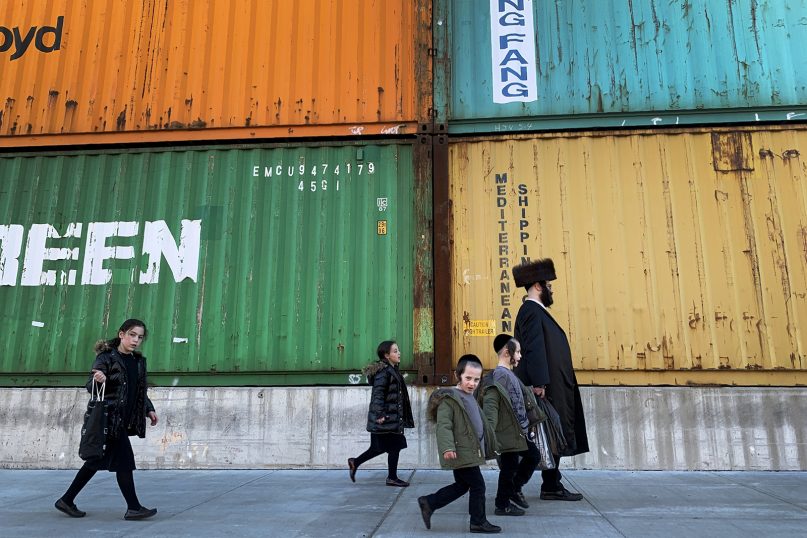 In this Tuesday, March 30, 2021, file photo, members of the Orthodox Jewish community walk past shipping containers in the South Williamsburg neighborhood of Brooklyn, New York. (AP Photo/Wong Maye-E)