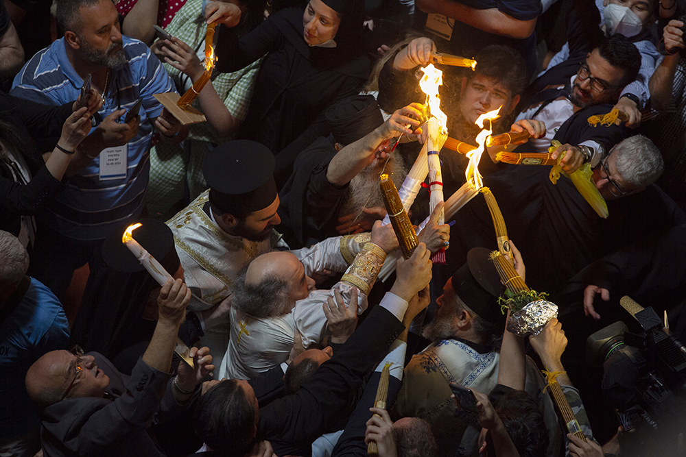 Greek Orthodox Patriarch of Jerusalem Theophilos III, center left, holds candles for Christian pilgrims during the ceremony of the Holy Fire at Church of the Holy Sepulchre, in the Old City of Jerusalem, Saturday, May 1, 2021. Hundreds of Christian worshippers took use of Israel's easing of coronavirus restrictions Saturday and packed a Jerusalem church revered as the site of Jesus' crucifixion and resurrection for an ancient fire ceremony ahead of Orthodox Easter. (AP Photo/Ariel Schalit)
