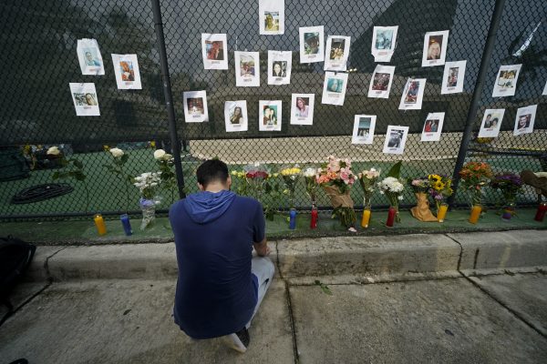 Leo Soto, who created this memorial with grocery stores donating flowers and candles, pauses in front of photos of some of the missing people that he put on a fence, near the site of an oceanfront condo building that partially collapsed in Surfside, Florida, June 25, 2021. (AP Photo/Gerald Herbert)