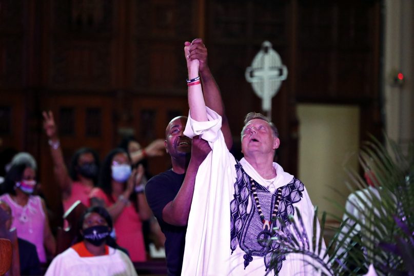 A parishioner raises Rev. Michael Pfleger's arm as he conducts his first Sunday church service as a senior pastor at St. Sabina Catholic Church following his reinstatement by Archdiocese of Chicago after decades-old sexual abuse allegations against minors, Sunday, June 6, 2021, in the Auburn Gresham neighborhood in Chicago. (AP Photo/Shafkat Anowar)