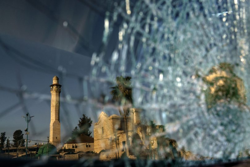 The minaret of the Al-Omari mosque and St. George Greek Orthodox Church are reflected in the broken windshield of a vehicle sitting outside a synagogue in the mixed Arab-Jewish town of Lod, central Israel, on May 26, 2021, in the wake of clashes between Arabs, police and Jews. The church shares a wall with a mosque and sits across from a synagogue in an area known as the triangle of religions. Like Jews and Arabs across the country, communities in Lod are on edge as the future of peaceful coexistence in mixed cities remains in question. (AP Photo/David Goldman)