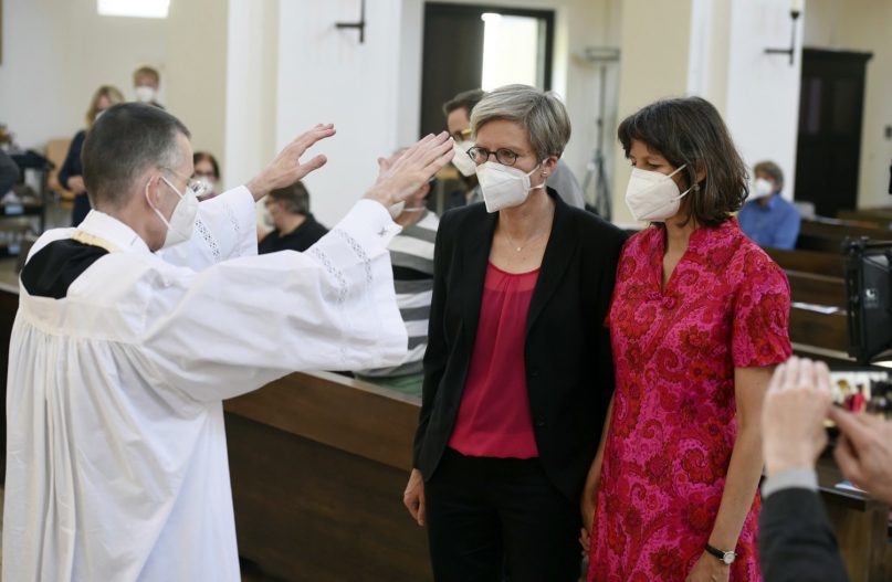 Vicar Wolfgang Rothe, left, blesses the couple Christine Walter, center, and Almut Muenster, right, during a Catholic service with the blessing of same-sex couples in St. Benedict's Church in Munich, May 9, 2021. Germany’s Catholic progressives are openly defying a recent Holy See pronouncement that priests cannot bless same-sex unions by offering exactly such blessings at services in about 100 different churches all over the country. The blessings at open worship services are the latest pushback from German Catholics against a document released in March by the Vatican’s orthodoxy office, which said Catholic clergy cannot bless same-sex unions. (Felix Hoerhager/dpa via AP)