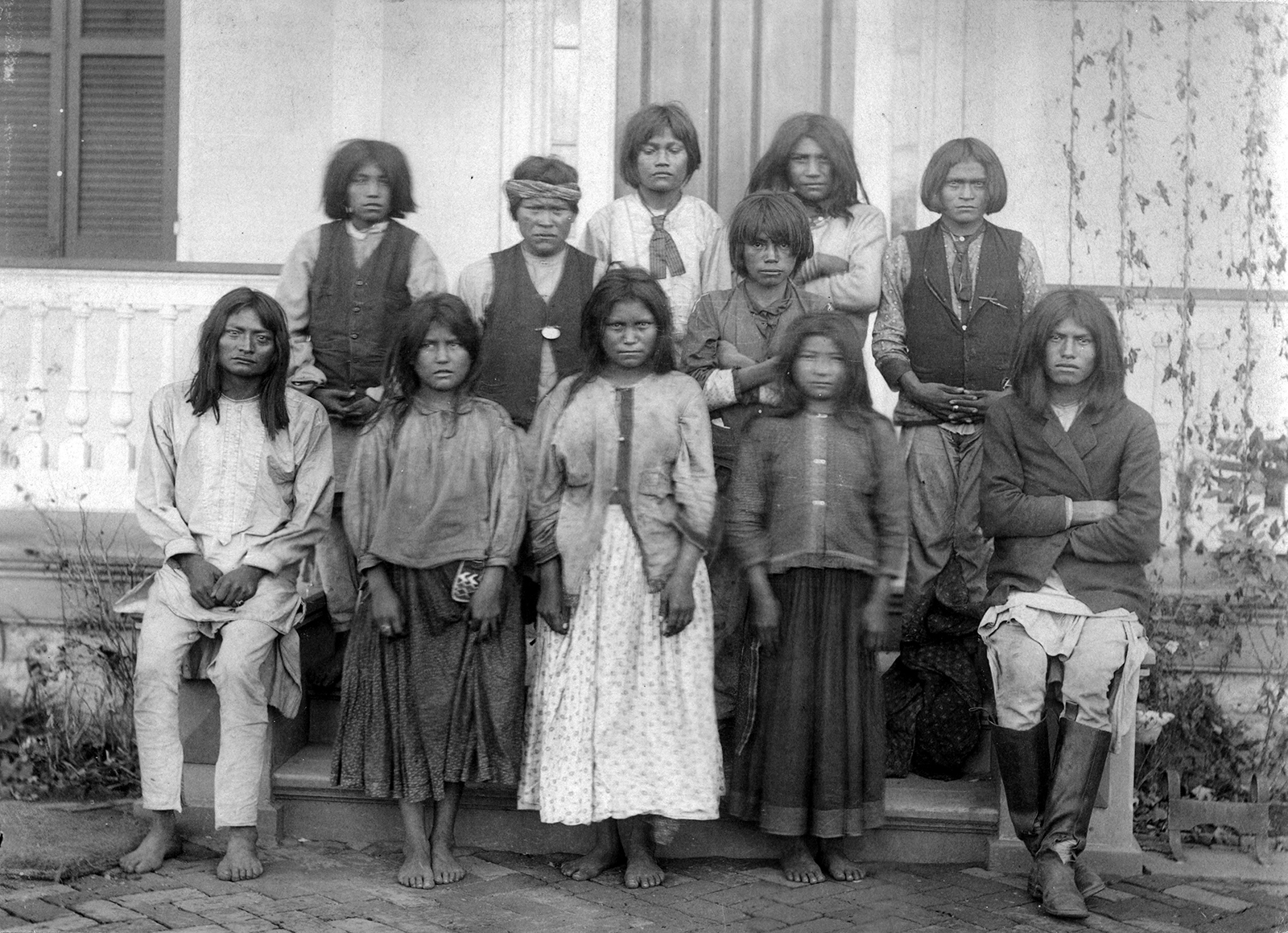 Meninos e meninas nativos americanos (Chiricahua Apache) posam ao ar livre na Carlisle Indian Industrial School em Carlisle, Pensilvânia, após sua chegada de Fort Marion, Flórida, em novembro de 1886. (Foto de JN Choate/Creative Commons)