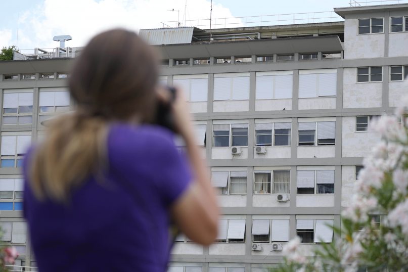 A press photographer aims her lens at the 10th floor of the Agostino Gemelli hospital, where Pope Francis was hospitalized Sunday, in Rome, Friday, July 9, 2021. The Vatican says Pope Francis is walking, working and has celebrated Mass at a Rome hospital where he also will deliver his Sunday weekly blessing while recovering from intestinal surgery.  (AP Photo/Gregorio Borgia)