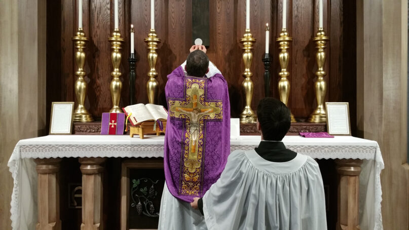 A priest elevates the Eucharist after consecrating it during a Latin Mass. Photo by Andrew Gardner/Creative Commons