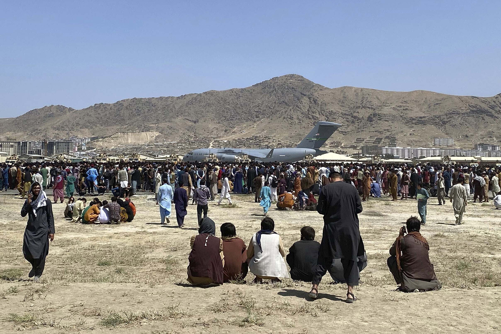 In this Aug. 16, 2021, file photo, hundreds of people gather near a U.S. Air Force C-17 transport plane along the perimeter at the international airport in Kabul, Afghanistan. After the Taliban takeover, employees of the collapsed government, civil society activists and women are among the at-risk Afghans who have gone into hiding or are staying off the streets. They hope for a way to leave their homeland. (AP Photo/Shekib Rahmani, File)
