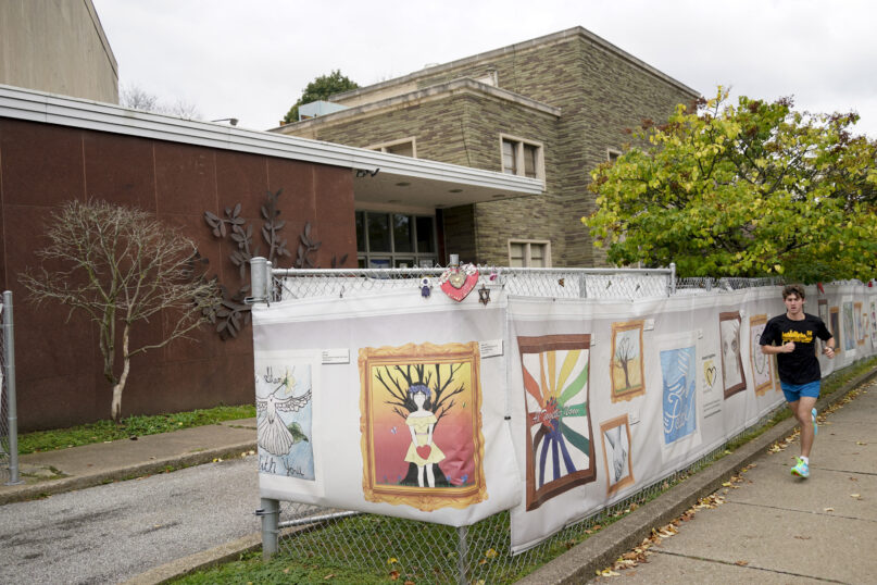 This photo from Oct. 16, 2021, shows the dormant landmark Tree of Life synagogue as a man jogs past the fencing with artwork submitted by Pittsburgh area school students in Pittsburgh's Squirrel Hill neighborhood. Renowned architect Daniel Libeskind is among those working to transform the site to share space with the Holocaust Center of Pittsburgh. The goal to create a solemn memorial as well as a place of regular activity is underway as the date marking the third year since 11 people were killed in America's deadliest antisemitic attack on Oct. 27, 2018 approaches. (AP Photo/Keith Srakocic)