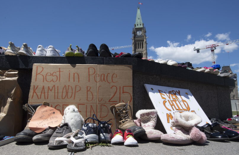 FILE - In this May 31, 2021 file photo, shoes sit on the Eternal flame memorial in recognition of the discovery of children's remains at the site of a former residential school in Kamloops, British Columbia, on parliament hill in Ottawa, Ontario. The Vatican announced Wednesday, Oct. 27, 2021 that Pope Francis has agreed to visit Canada to help ongoing efforts at reconciliation with Indigenous peoples following shocking revelations of the Catholic church's role in the abuse and deaths of thousands of native children. (Adrian Wyld/The Canadian Press via AP, file)