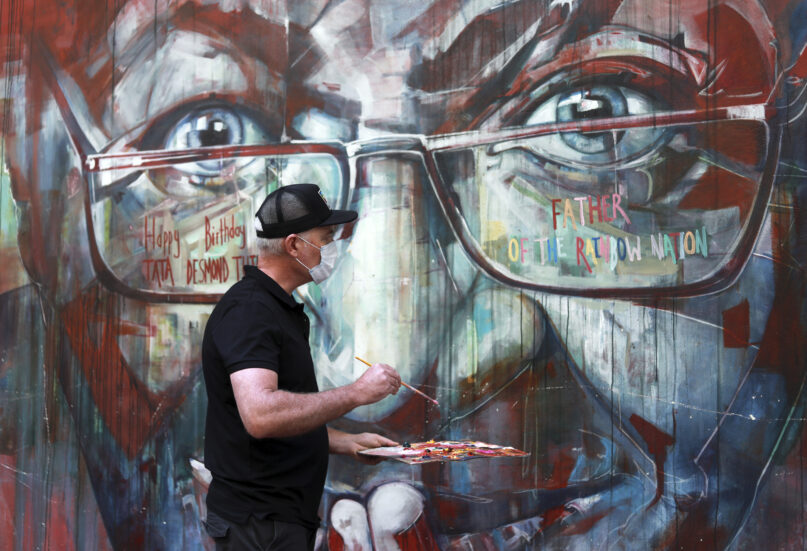 A wall mural, depicting Anglican Archbishop Emeritus, Desmond Tutu, is restored by the artist Brian Rolfe after it was defaced, in Cape Town, South Africa, Thursday Oct. 7, 2021. As South Africa's anti-apartheid icon, Tutu turns 90, recent racist graffiti on the wall mural portrait highlights the continuing relevance of his work for equality. (AP Photo/Nardus Engelbrecht)