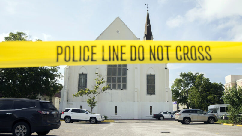 FILE - In this June 19, 2015 file photo, police tape surrounds the parking lot behind the AME Emanuel Church as FBI forensic experts work the crime scene, in Charleston, S.C. Families of nine victims killed in a racist attack at the church have reached a settlement with the Justice Department over a faulty background check that allowed Dylann Roof to purchase the gun he used in the 2015 massacre. (AP Photo/Stephen B. Morton, File)