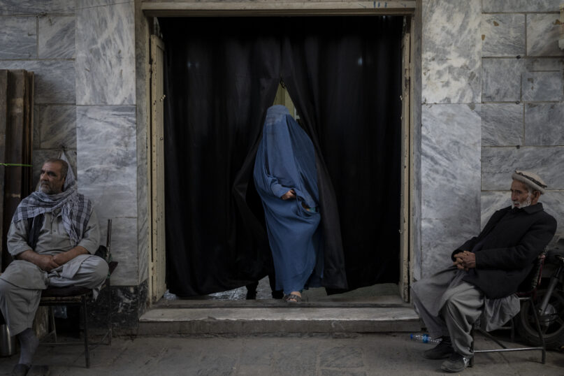 A woman leaves a Shiite shrine in a predominantly Hazara neighborhood while two men stand guard in Kabul, Afghanistan, Tuesday, Nov. 9, 2021. A strange, new relationship is developing in Afghanistan following the takeover by the Taliban three months ago. The Taliban, Sunni hard-liners who for decades targeted the Hazaras as heretics, are now their only protection against a more brutal enemy: the Islamic State group. (AP Photo/Bram Janssen)